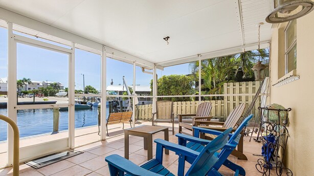 Un patio techado con sillas Adirondack azules, una mesita y vista al puerto deportivo.