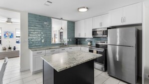 Una cocina moderna con armarios blancos, encimera de granito, electrodomésticos de acero inoxidable y salpicadero color aguamarina.