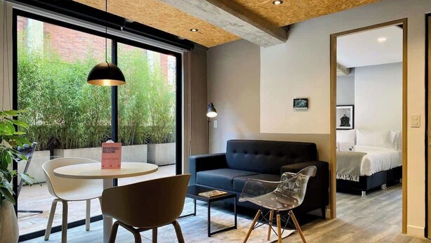 Una sala moderna con una mesa redonda, dos sillas, un sofá y una mesita de centro. Hay un ventanal con vistas a zonas verdes.