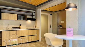 Una cocina moderna con armarios de madera, un microondas y una silla transparente. Hay una mesa blanca con un cartel de bienvenida en rosa.