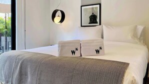 Una habitación de hotel moderna con una cama grande, un reloj de pared redondo, un cuadro enmarcado y vistas al balcón.