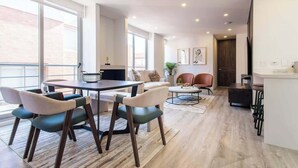 Ein modernes Wohnzimmer mit Essbereich, großen Fenstern und einer Küche.