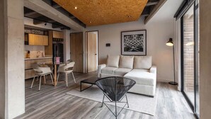 Ein modernes Wohnzimmer mit einer Couch, einem Esstisch mit Stühlen, einem schwarzen Sessel und einem großen Fenster.