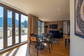 A spacious living area with a large sliding glass door leading to a balcony, a round dining table with chairs, a sofa, and a flat-screen TV mounted on a brick wall. - NOK Stylish 2 Masters w/Patio & View (Bogotá)