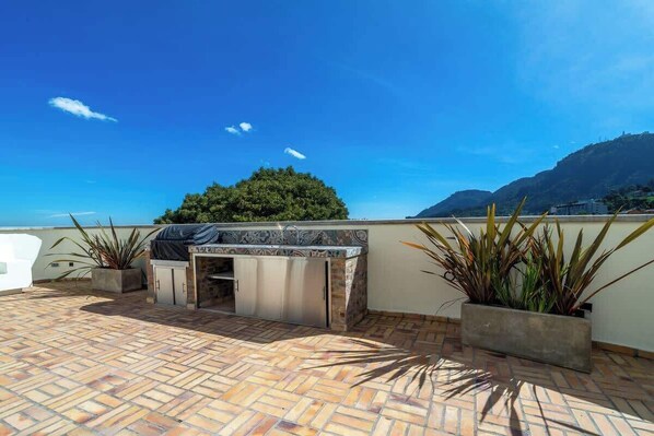 Terraza en la azotea con zona de barbacoa, plantas en macetas y vistas a las montañas.
