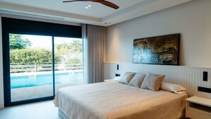 Quarto com uma cama grande, ventoinha no teto, um quadro e vista para uma piscina.