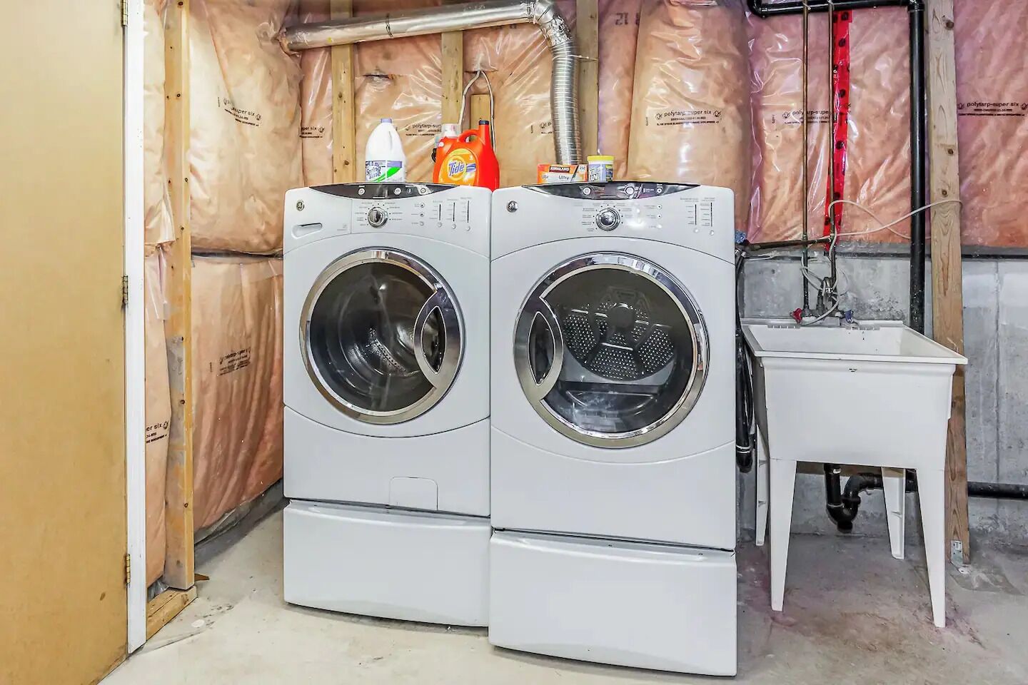 A laundry room with two stacked front-loading washing machines, a small table, and insulation on the walls.