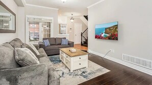 A living room with a gray sectional sofa, a white coffee table, and a large painting of a coastal landscape.