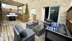 An outdoor patio with wicker furniture, a grill, and a wooden pergola.