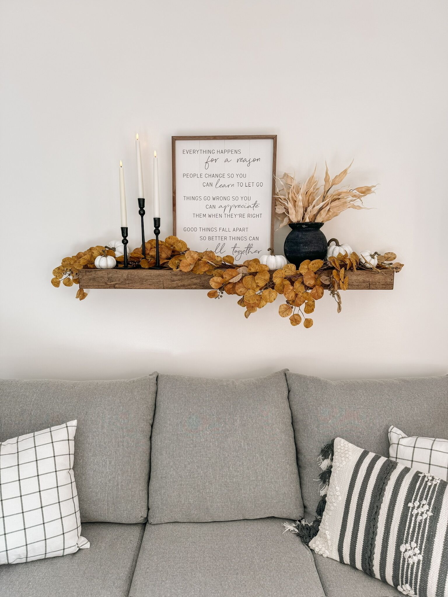 A cozy living room with a gray sofa, decorative wall shelf, and a framed inspirational quote.