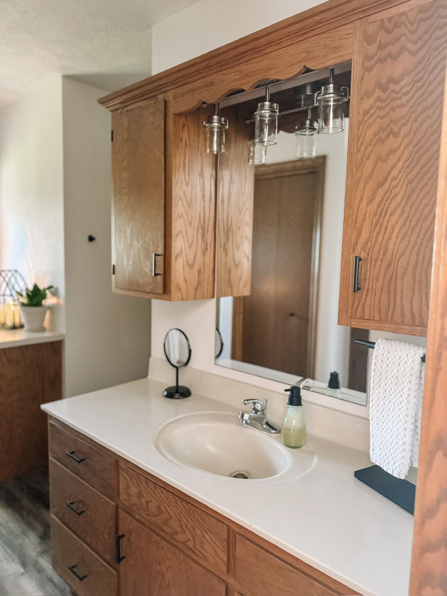 Un baño con armarios de madera, un lavabo blanco, un espejo y un perchero para toallas.