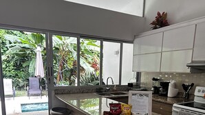 A modern kitchen with a central island, bar stools, and a view of a pool and greenery outside. - Charming 3-bedroom condo with pool, AC, WiFi in peaceful Herradura, pet friendly (Herradura)