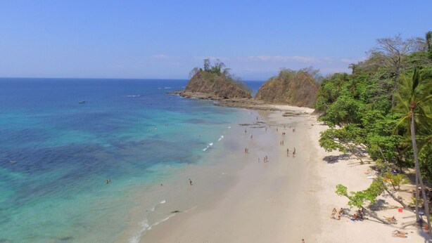 A beach with clear turquoise waters, people swimming and sunbathing, and lush greenery on the right. - Charming 3-bedroom condo with pool, AC, WiFi in peaceful Herradura, pet friendly (Herradura)