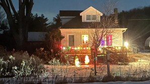 Ein Haus mit einem gut beleuchteten Veranda, einem abgestellten Wohnmobil und einem mit Schnee bedeckten Boden.
