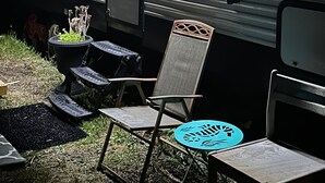 Ein stehender Wohnmobil mit Tür, Fenstern und einem kleinen Tisch mit Stühlen davor.