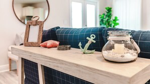 A wooden table with a mirror, a candle jar, and decorative items in a living room with a blue couch and a plant. - 5BR WindMark Beach Bunk Room, Pools, Golf Cart, Ping Pong  (Port St. Joe)