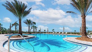 A swimming pool with a curved design, surrounded by palm trees and a clear blue sky. - 5BR WindMark Beach Bunk Room, Pools, Golf Cart, Ping Pong  (Port St. Joe)