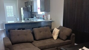 A modern living room with a sectional sofa, a coffee table, and a kitchen area in the background. - Sweet Home 5 (Franklin)