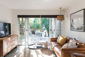 Un soggiorno moderno con televisione, divano, tavolino e vista su un giardino tramite porte in vetro.