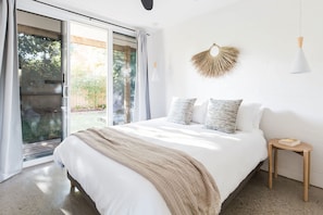 A bedroom with a bed, a bedside table, a wall-mounted light fixture, and a view through a glass door.