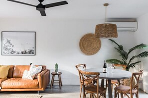Un soggiorno moderno con un divano in pelle, un tavolo da pranzo rotondo con sedie, una ventola a soffitto e un condizionatore d'aria a parete.