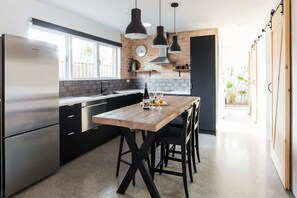 A modern kitchen with a wooden island, black cabinets, stainless steel appliances, pendant lights, and a view to the outside. - The Sunshine Bungalow Beautiful Noosa Home (Noosa)