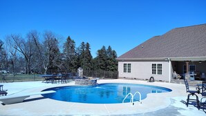 Ein Swimmingpool mit einer Wand aus Natursteinen, umgeben von einem Zaun und Bäumen.