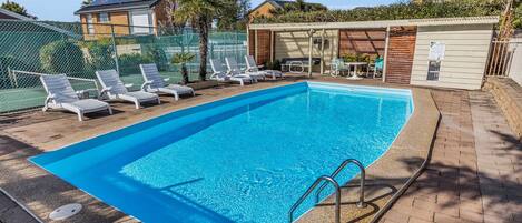 Una piscina rectangular con borde azul, rodeada de sillas de descanso y una zona de estar techada.