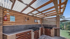 Zona de cocina exterior con una pérgola de madera, un extintor y un cartel que indica zona para fumadores.