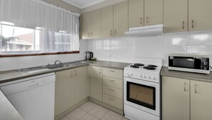 Una cocina con gabinetes color beige, lavavajillas, estufa y microondas.