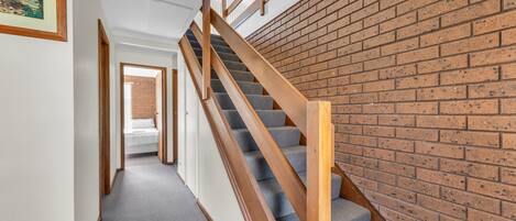 A staircase with wooden railings and carpeted steps leading to a room with a brick wall.