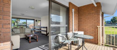 A balcony with a glass door leading to a living area, furnished with a sofa, coffee table, and chairs.