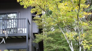 A wooden pathway leading to a modern building with large windows and a balcony. - KAMATA SANSO (Hakuba)