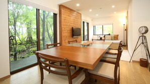 A modern dining room with a wooden table and chairs, a television, and a view of the outdoors. - KAMATA SANSO (Hakuba)