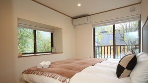 A bedroom with a large bed, a window with blinds, and a view of the outside. - KAMATA SANSO (Hakuba)