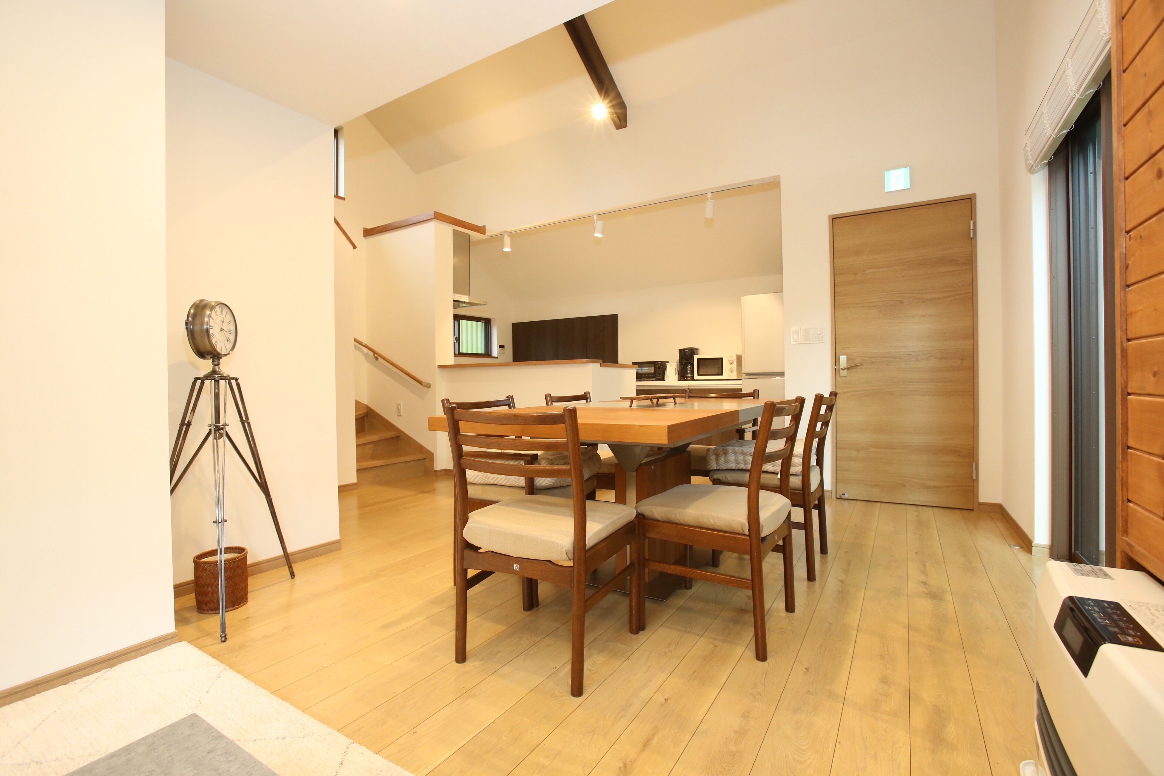 A modern dining area with a wooden table and chairs, a tripod, and a staircase leading to another room.
