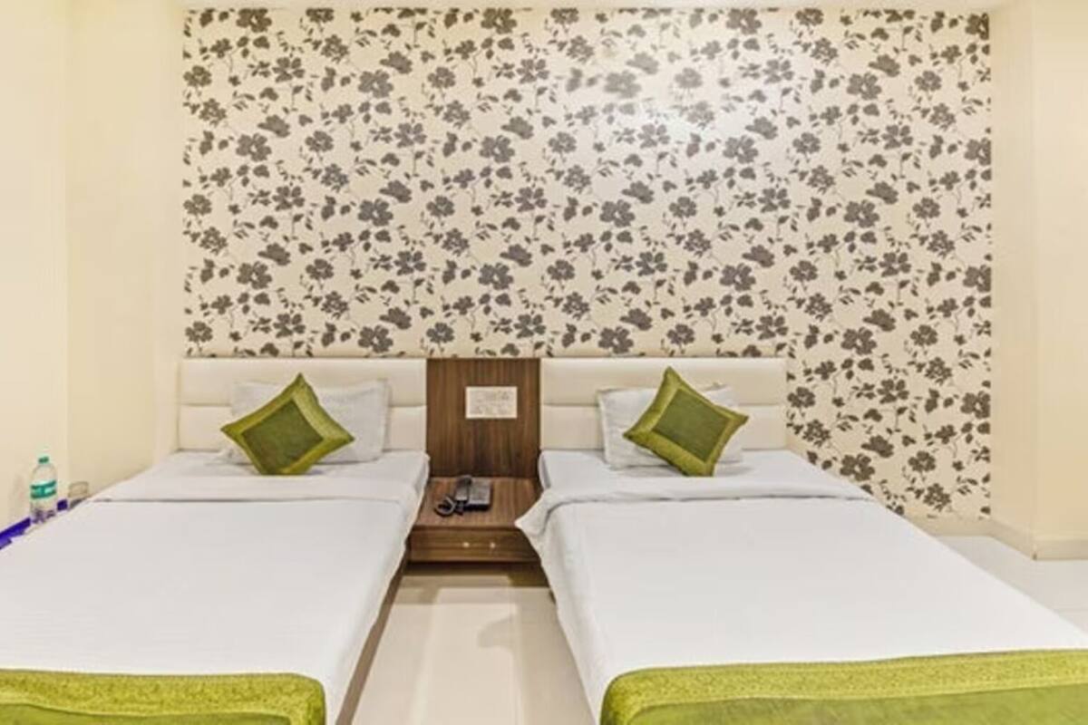 Ein Doppelzimmer mit blumigem Wandpapier, zwei grünen Kissen und einem Nachttisch mit Lampe.