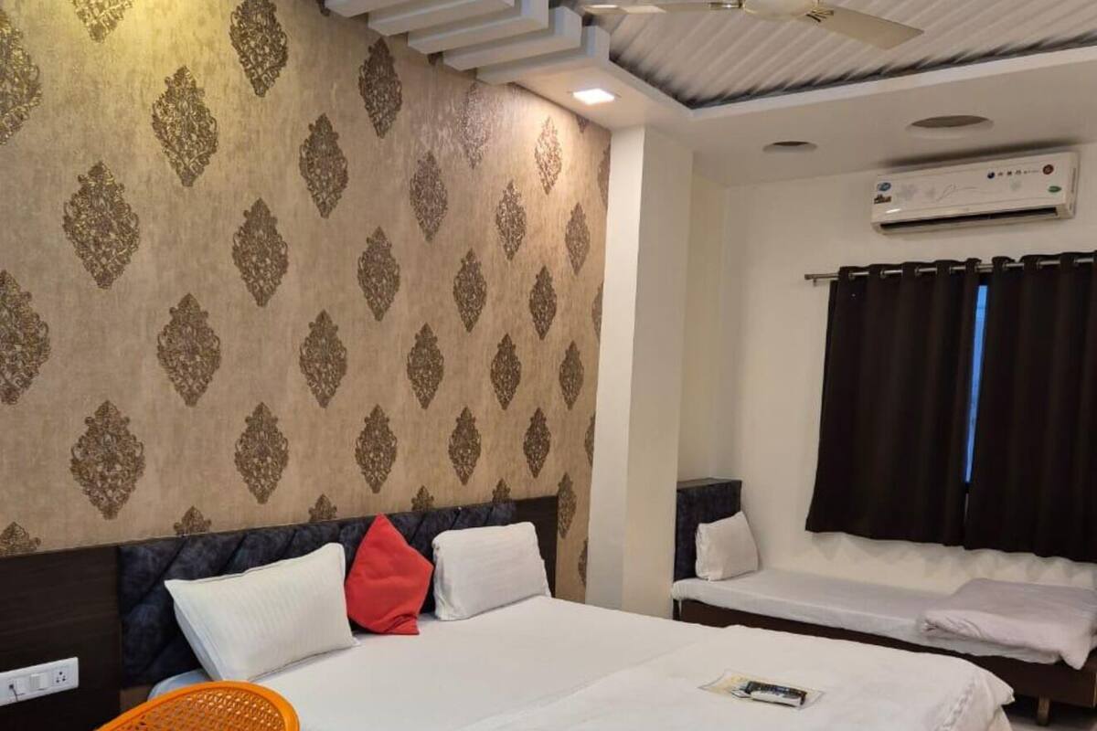 A hotel room with a large bed, a desk, and a chair. There is a ceiling fan and an air conditioning unit on the wall.