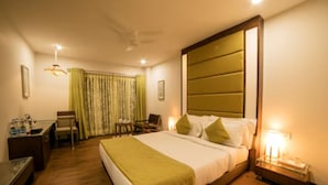 A hotel room with a large bed, bedside tables, a desk with a chair, a desk lamp, and curtains. - Hotel Shree Aaradhy (Ujjain)