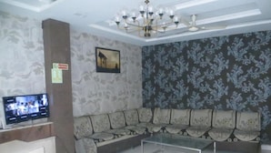 A living room with a sofa, a coffee table, a TV, and a patterned wall. - Hotel Shree Aaradhy (Ujjain)