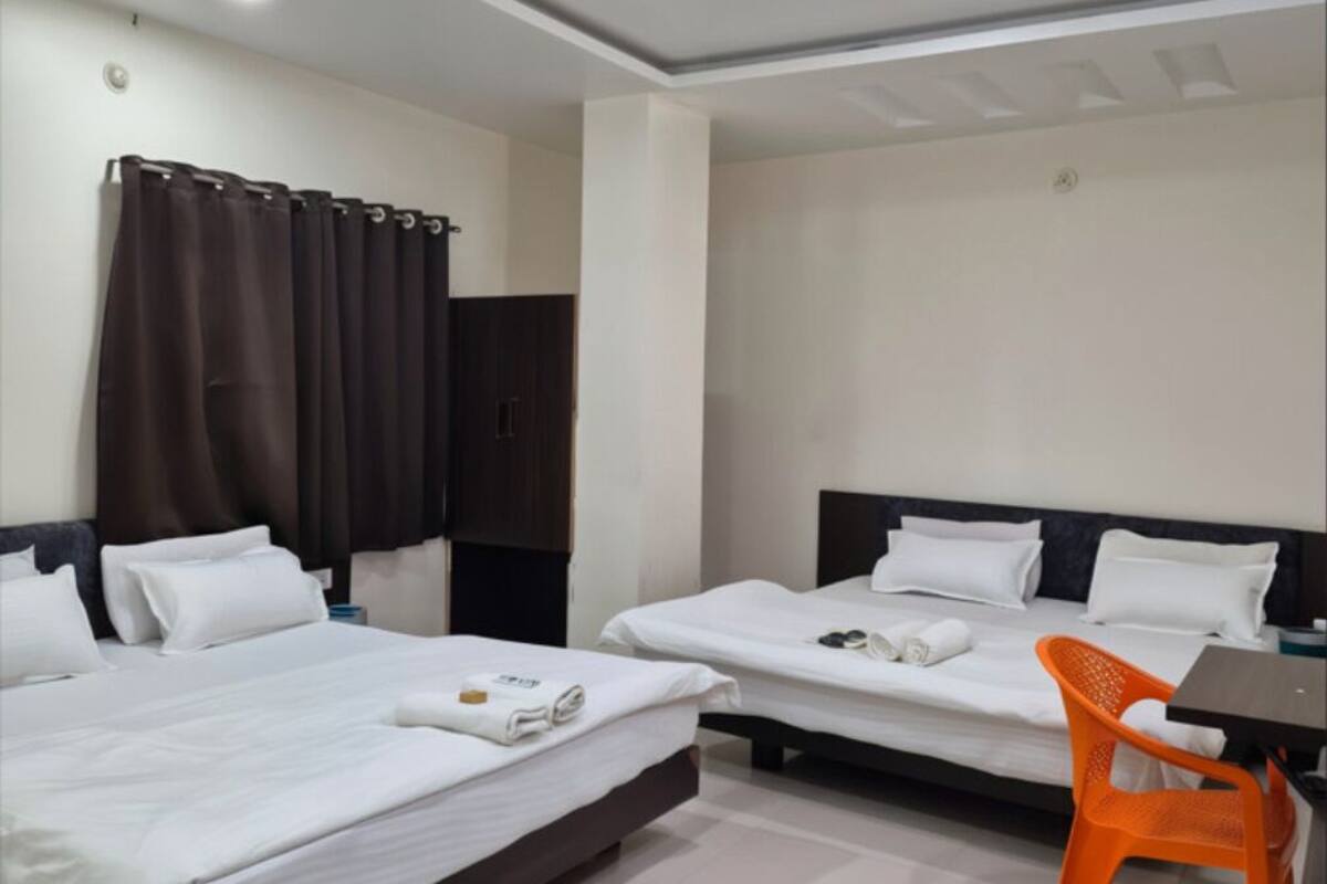 A hotel room with two beds, a ceiling fan, a desk with a chair, and a window with curtains.