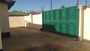 Une cour dallée, avec un portail vert, des murs blancs et un toit recouvert de tuiles.