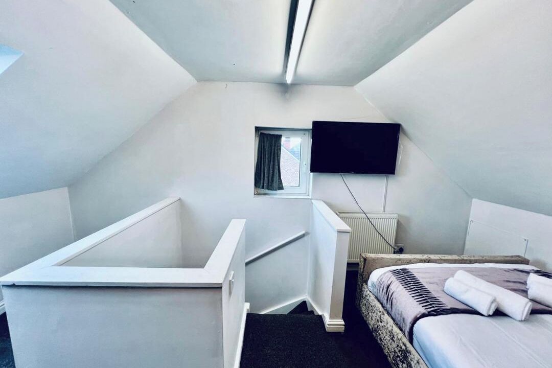 A small, triangular room with a single bed, a small window, a flat-screen TV mounted on the wall, and a white bathtub.