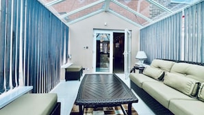 A sunlit patio with a glass ceiling, a beige sofa, a woven table, and a patterned rug. - 13 Guests - Free Parking - Manchester House (Manchester)