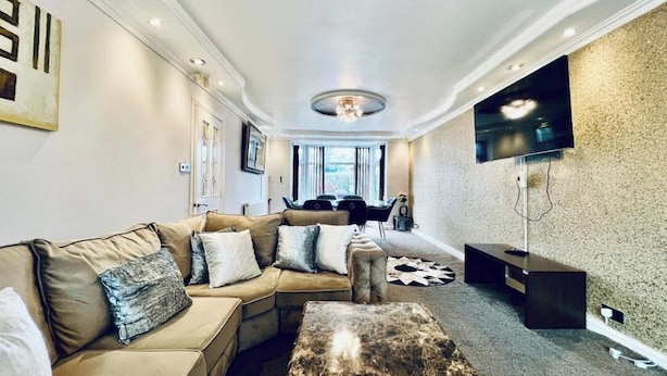 A modern living room with a sectional sofa, a coffee table, and a flat-screen TV mounted on a textured wall. - 13 Guests - Free Parking - Manchester House (Manchester)
