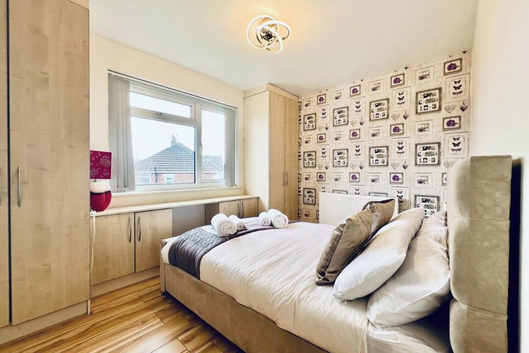 Une chambre à coucher avec un lit, une fenêtre, un plancher en bois et un mur orné de tableaux encadrés.