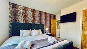 A hotel room with a large bed, a television mounted on the wall, and a door leading to another room. - 13 Guests - Free Parking - Manchester House (Manchester)