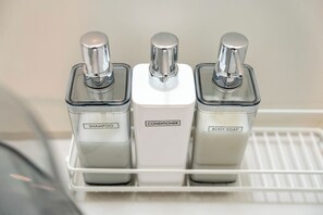 Ein Badezimmerschrank mit drei Toilettenartikeln, beschriftet mit Shampoo, Conditioner und Duschseife.