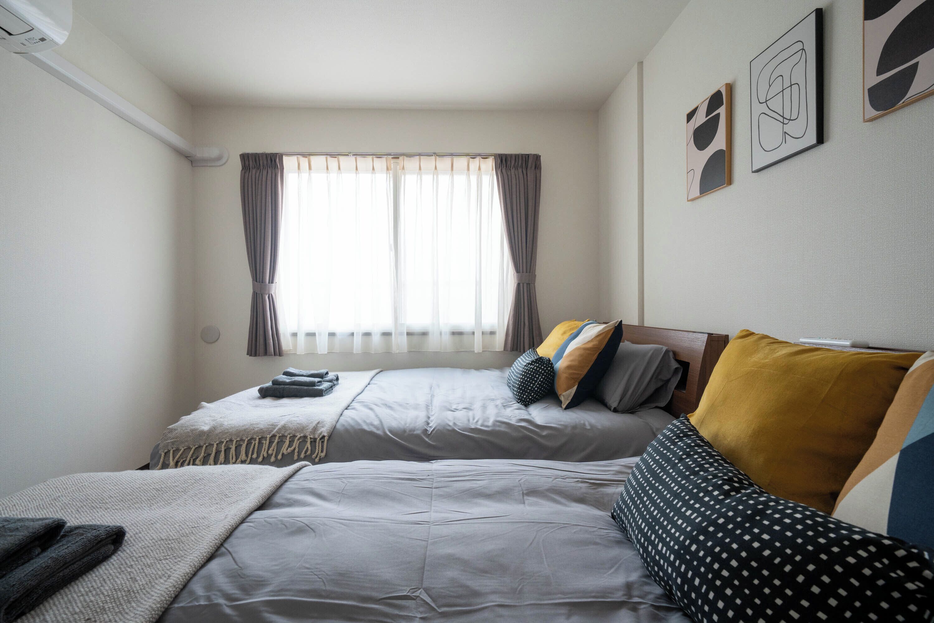 Une chambre d’hôtel avec deux lits, une fenêtre avec des rideaux et des œuvres d’art accrochées au mur.