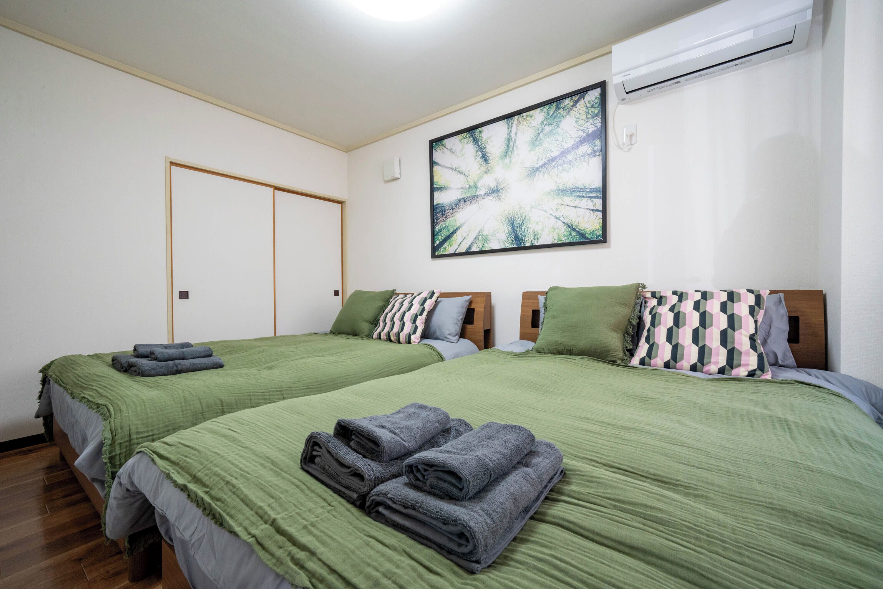 A hotel room with two beds, green bedding, and a large abstract painting on the wall.